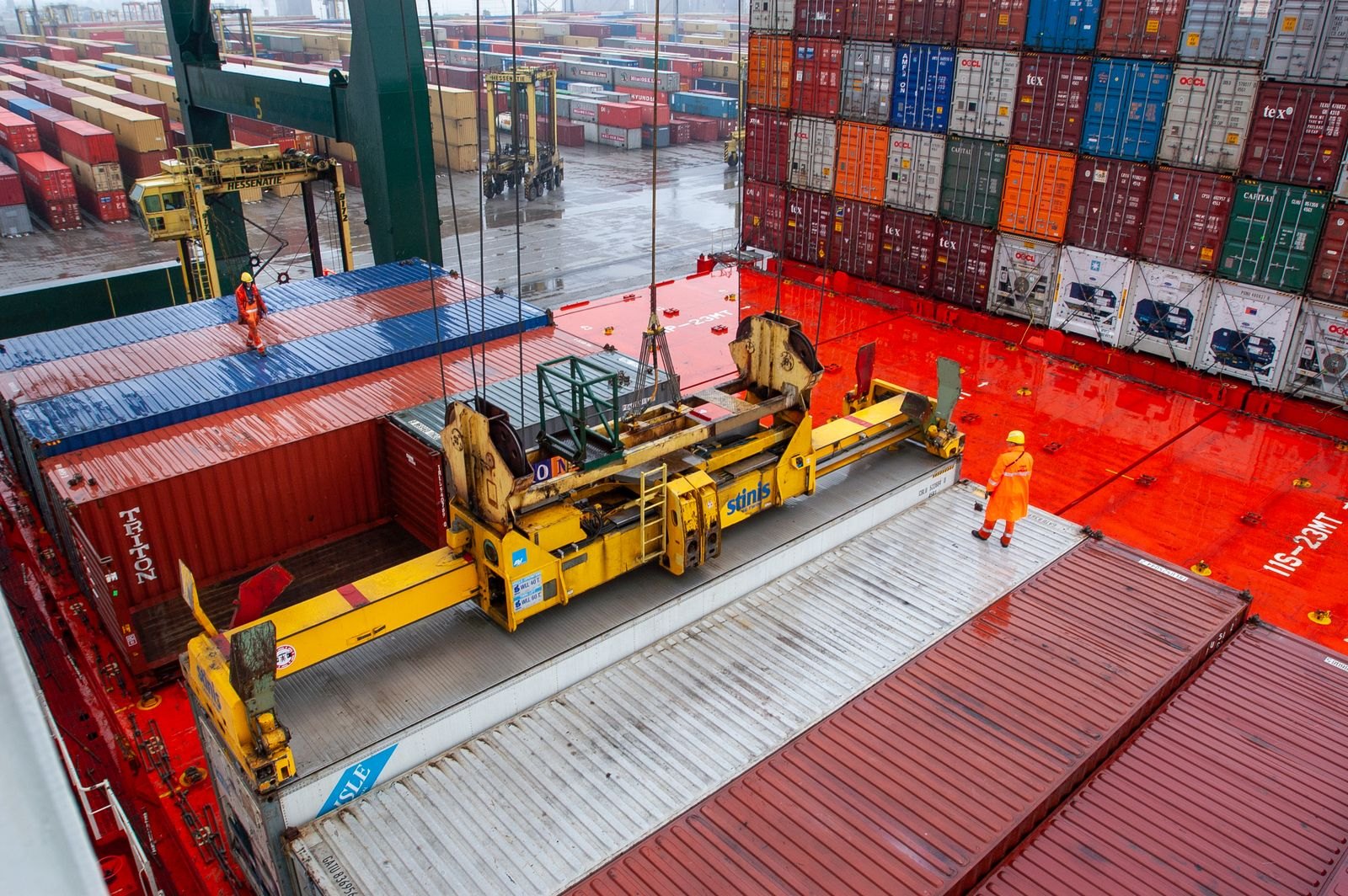 Port workers and container equipment beside a cargo vessel